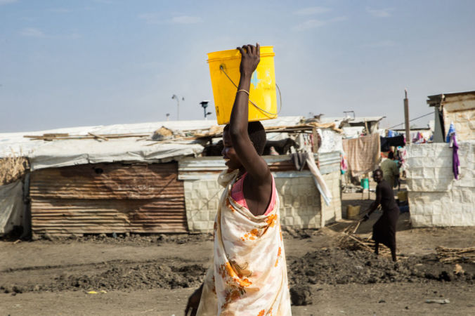A woman carries a bucket of water in the Malakal Protection of Civilian (PoC) site, in north-east South Sudan. Photo by Igor Barbero/MSF.